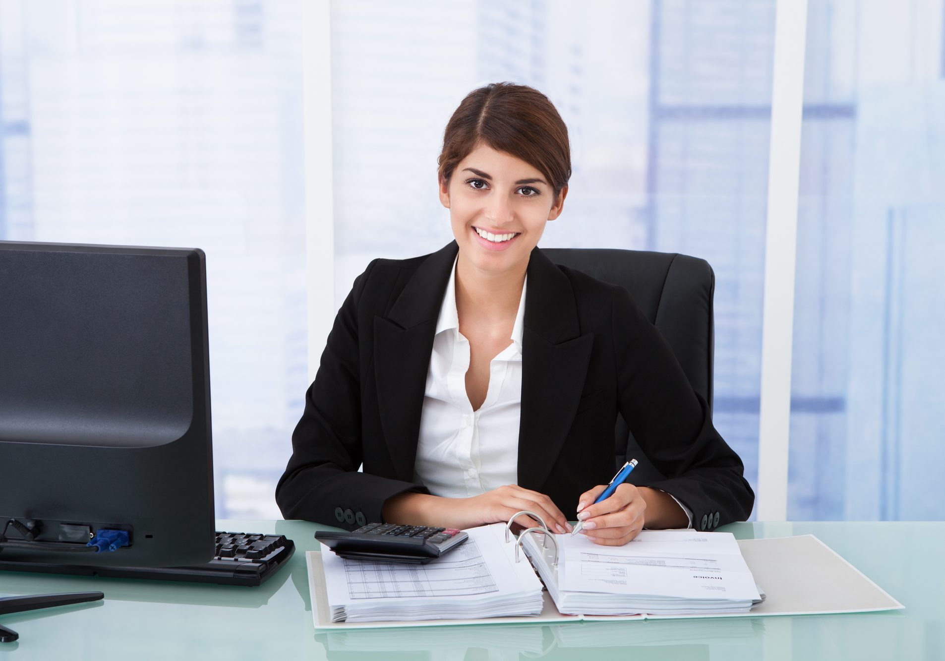 Portrait of confident young businesswoman using calculator at office desk